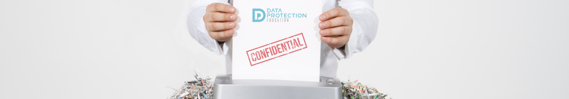 Hands of a man putting some paper marked confidential through a shredder sitting on a pile of shredding. Data Protection Education logo.